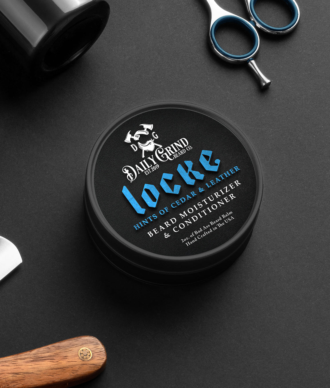 Daily Grind Locke Beard Balm in Cedar and Leather scent, beard conditioner and moisturizer for men shown in a black tin on a grooming table